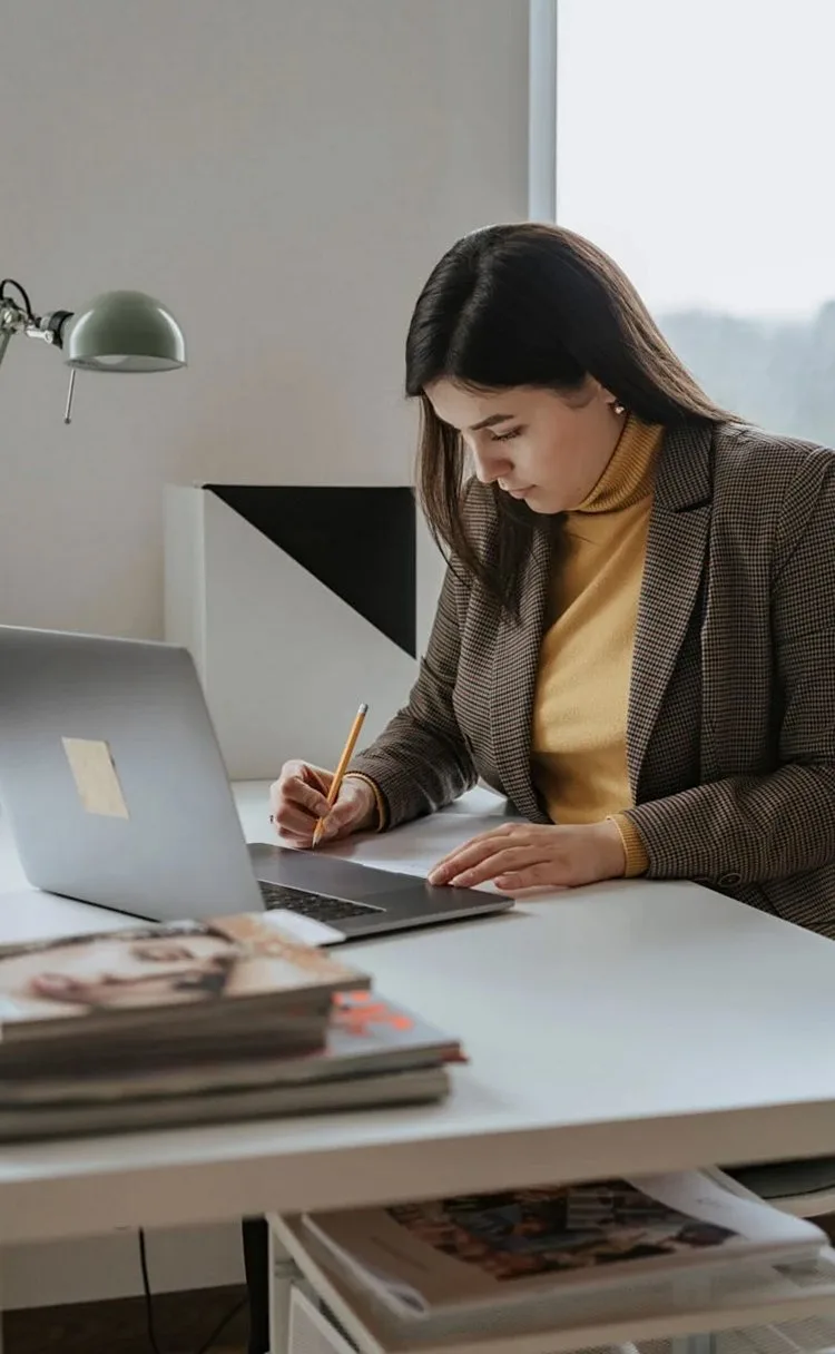 Woman at a desk with a laptop and printed magazines, working through notes